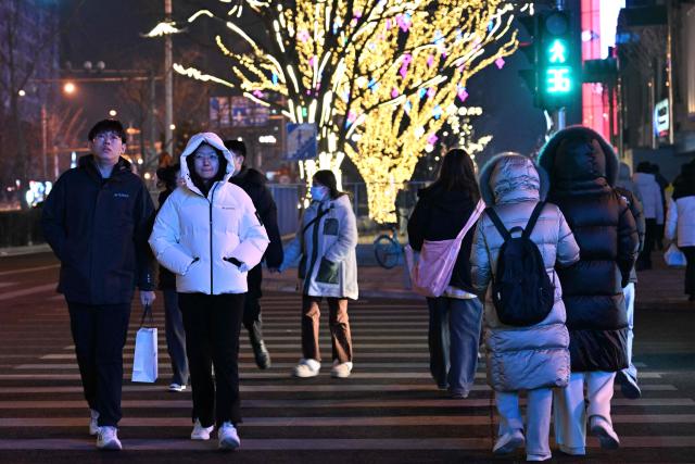 People walk across a road in Beijing on December 28, 2025. (Photo by ADEK BERRY / AFP)