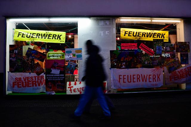 People walk past an illuminated fireworks shop in Berlin on December 28, 2025. (Photo by Tobias SCHWARZ / AFP)