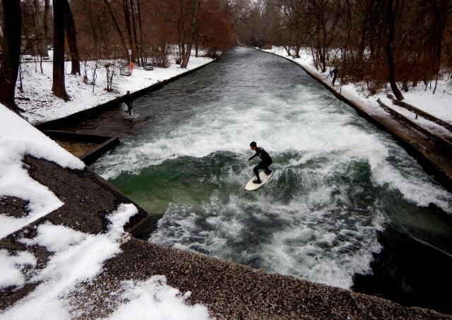 (FILES) Surfers ride the Eisbach (ice creek) wave during freezing conditions on the Isar River in the English Garden in Munich, southern Germany on January 4, 2017. A temporary ramp installed in Munich's Eisbach, which had provisionally restored the famous surfing wave, has been removed by the fire brigade on December 28, 2025, according to a spokesperson. The wave had disappeared in October 2025 after cleaning works of the creek bed. (Photo by Mark RALSTON / AFP)