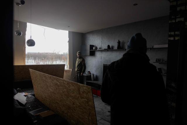 People stand next to plywood boards for damaged windows in a damaged residential building following Russian drones and missiles attack, in Kyiv, on December 28, 2025, amid the Russian invasion in Ukraine. A Russian drone and missile barrage on Kyiv and its suburbs killed one person, wounded two dozen and cut off heating and electricity for hundreds of thousands of people left in freezing temperatures on December 27, 2025. (Photo by Tetiana DZHAFAROVA / AFP)