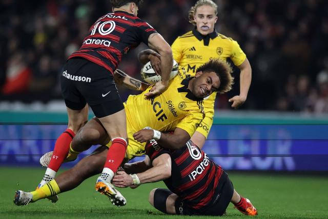 La Rochelle's French centre Simeli Daunivucu (C) is tackled by Toulouse's English flanker Jack Willis (R) and Toulouse's French fly-half Romain Ntamack (L) during the French Top 14 rugby union match between Stade Toulousain and Stade Rochelais (La Rochelle) at the TFC Stadium in Toulouse, southwestern France, on December 28, 2025. (Photo by Valentine CHAPUIS / AFP)