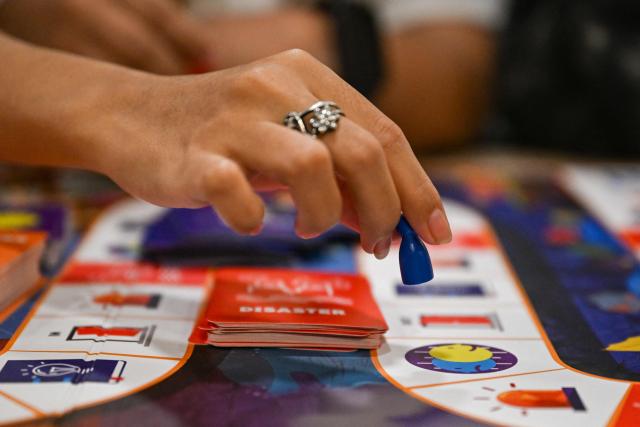 This photo taken on December 9, 2025, shows participants playing Master of Disaster, a board game about disaster preparedness, at a library in Valenzuela, Metro Manila. In a library in the Philippines, a die rattles on the surface of a board before coming to a stop, putting one of its players directly in the path of a powerful typhoon. (Photo by Jam STA ROSA / AFP) / TO GO WITH STORY: Philippines-environment-disaster-climate-game, FOCUS by Pam CASTRO