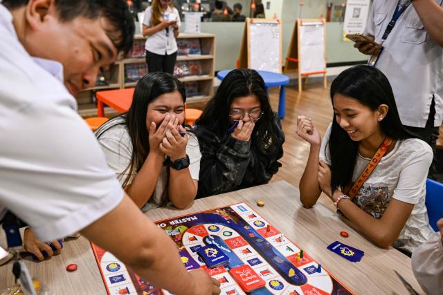 This photo taken on December 9, 2025, shows participants playing Master of Disaster, a board game about disaster preparedness, at a library in Valenzuela, Metro Manila. In a library in the Philippines, a die rattles on the surface of a board before coming to a stop, putting one of its players directly in the path of a powerful typhoon. (Photo by Jam STA ROSA / AFP) / TO GO WITH STORY: Philippines-environment-disaster-climate-game, FOCUS by Pam CASTRO