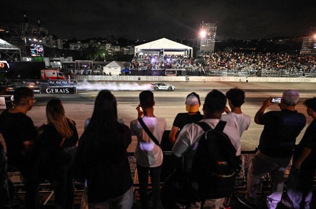 Attendees watch a Porsche racing during a car exhibition at La Carlota air base in Caracas on December 28, 2025. (Photo by Juan BARRETO / AFP)