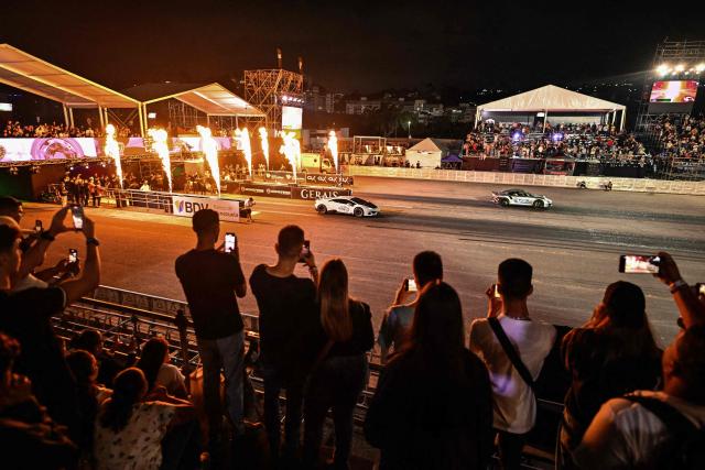 Attendees watch a Porsche and Lamborghini racing during a car exhibition at La Carlota air base in Caracas on December 28, 2025. (Photo by Juan BARRETO / AFP)