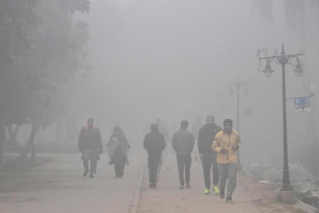People jog across a park amid dense smog in Lahore on December 29, 2025. (Photo by Arif ALI / AFP)