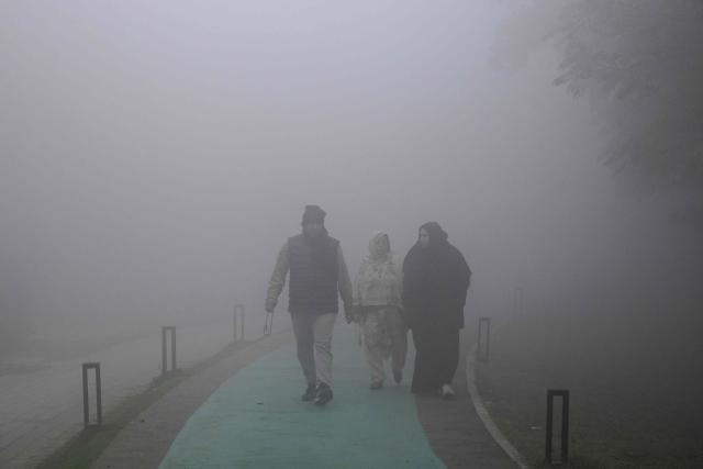 People walk across a park amid dense smog in Lahore on December 29, 2025. (Photo by Arif ALI / AFP)