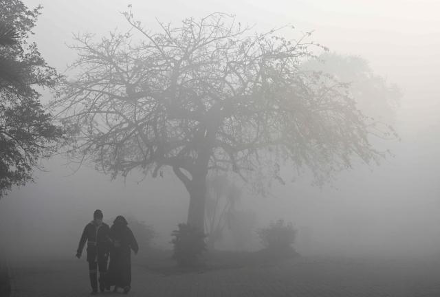 People walk across a park amid dense smog in Lahore on December 29, 2025. (Photo by Arif ALI / AFP)
