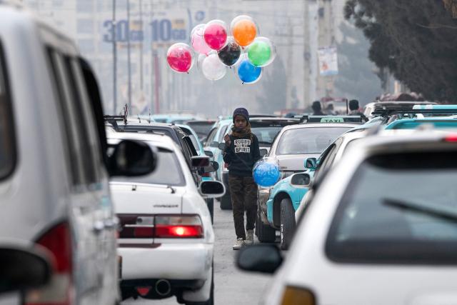 An Afghan balloon vendor wades through traffic as he looks for customers along a busy street in Kabul on December 29, 2025. (Photo by Wakil KOHSAR / AFP)