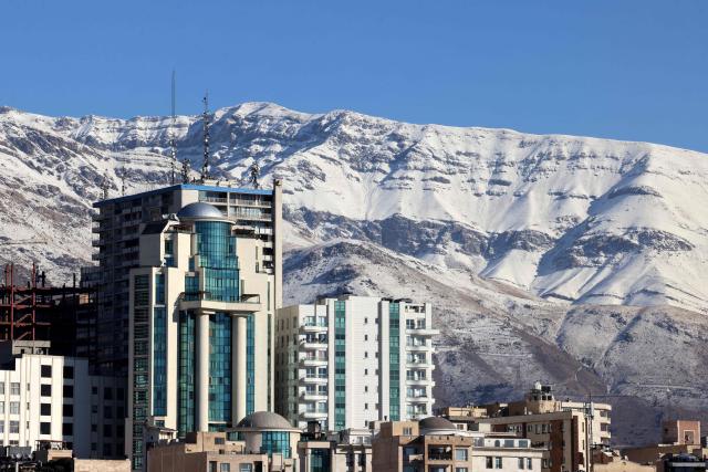 A photograph shows buildings in the Iranian capital Tehran with the snow-covered Alborz mountain range in the background on December 29, 2025. Tehran has seen intermittent rain since early December after months of dry weather, partially replenishing some of the city's reservoirs but leaving overall levels critically low. Iran, a largely arid country, has for years suffered chronic dry spells and heat waves, which are expected to worsen with climate change. (Photo by ATTA KENARE / AFP)