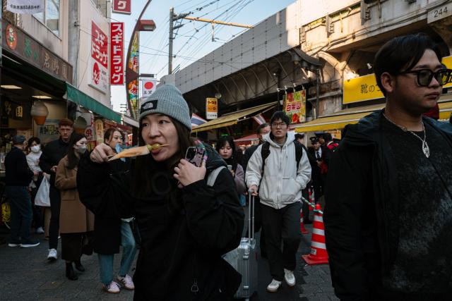 A pedestrian eats a snack as others throng the Ueno shopping district ahead of the new year in Tokyo on December 29, 2025. (Photo by Philip FONG / AFP)