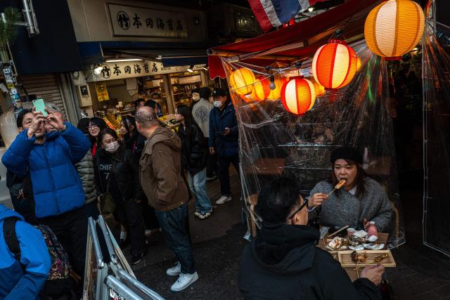 Diners (R) eat at a restaurant while pedestrians walk past and take pictures in Tokyo's Ueno shopping district on December 29, 2025. (Photo by Philip FONG / AFP)