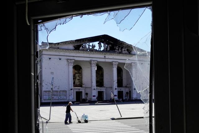 (FILES) A man carries the bottles with drinking water past the partially destroyed Mariupol drama theatre in the city of Mariupol on July 3, 2022, amid the ongoing Russian military action in Ukraine. A theatre that became one of the bombed out symbols of a Russian siege of the city of Mariupol in eastern Ukraine in 2022 has reopened after a huge redevelopment, Russian authorities have announced. (Photo by AFP)