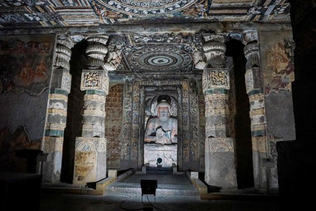 This photograph taken on December 14, 2025 shows a Buddha sculpture inside a rock-cut hall at the Ajanta Caves in Maharashtra. The Ajanta Caves are about 30 Buddhist cave monuments and temples that date from around the 2nd century BCE to around 480 CE, cut into the dark basalt rock of the Deccan Traps, the remnants of an immense volcanic event some 65 million years ago. The paintings and sculptures at the site are considered masterpieces of Buddhist religious art, according to UNESCO, which gave the caves World Heritage Site status in 1983. (Photo by Peter MARTELL / AFP)