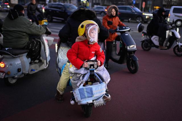 A child faces rearward while riding pillion on an electric bicycle in Beijing on December 29, 2025. (Photo by WANG Zhao / AFP)
