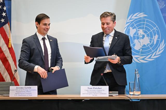 US Under Secretary of State for Foreign Assistance, Humanitarian Affairs and Religious Freedom Jeremy Lewin (L) and United Nations Under-Secretary-General for Humanitarian Affairs Tom Fletcher gesture after the signing ceremony of a $2 billion pledge of United States for United Nations humanitarian aid in 2026, at the US Mission in Geneva, on December 29, 2025. According to UN data, the United States remains the top humanitarian aid donor in the world, but that amount fell significantly in 2025 to $2.7 billion, down from around $11 billion in 2023 and 2024 and from over $14 billion in 2022. (Photo by Fabrice COFFRINI / AFP)