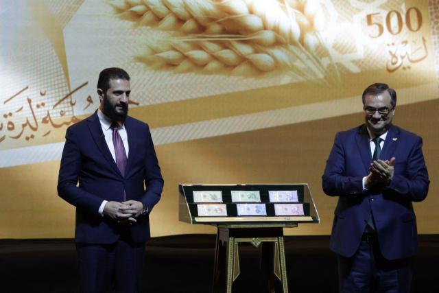 Syria's President Ahmed al-Sharaa (L) and Syria's Central bank chief Abdul Qadir al-Hasriya (R) stand between the country's new revamped currency notes at the Conference Palace in the Syrian capital Damascus on December 29, 2025. Syria's central bank chief said on December 25 that the country's currency would start to be replaced with a revamped version from January 1, as Damascus tries to relaunch its economy after emerging from the rule of ousted leader Bashar al-Assad last year. (Photo by Bakr ALkasem / AFP)