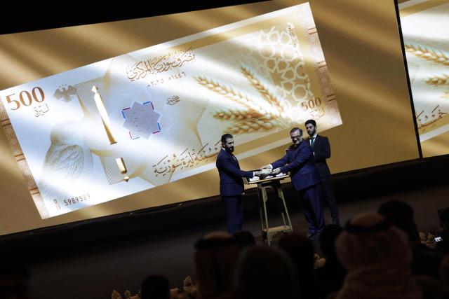 Syria's President Ahmed al-Sharaa (L) and Syria's Central bank chief Abdul Qadir al-Hasriya (R) hold one of the country's new revamped currency notes at the Conference Palace in the Syrian capital Damascus on December 29, 2025. Syria's central bank chief said on December 25 that the country's currency would start to be replaced with a revamped version from January 1, as Damascus tries to relaunch its economy after emerging from the rule of ousted leader Bashar al-Assad last year. (Photo by Bakr ALkasem / AFP)