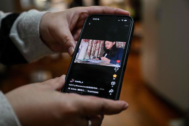 Xu Zoe, 40, mother of Estella, a homeschooled student, shows a video of her daughter during an interview with AFP in her home in Shanghai on November 25, 2025. They are among a small number of parents in China who are rethinking the country's rigorous education system, in which school days can last 10 hours, with students often working late into the evening on extra tutoring and homework. (Photo by Hector RETAMAL / AFP) / TO GO WITH: China-education-children-family, FOCUS by Mary YANG