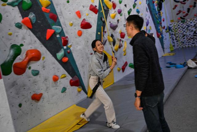 Estella, 14, a homeschooled student, looks at her father Shen while attending an indoor rock climbing in Shanghai on November 25, 2025. They are among a small number of parents in China who are rethinking the country's rigorous education system, in which school days can last 10 hours, with students often working late into the evening on extra tutoring and homework. (Photo by Hector RETAMAL / AFP) / TO GO WITH: China-education-children-family, FOCUS by Mary YANG