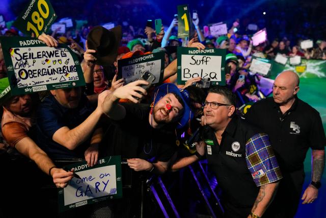 Scotland's Gary Anderson (2R) poses with supporters ahead of his match against Netherlands' Jermaine Wattimena during the World Darts Championship at the Alexandra Palace in London on December, 28, 2025. Dressed as Elvis, Asterix or Snow White, usually with a drink in hand, fans transform London's Alexandra Palace into an overheated darts temple for a world championship that resembles a Christmas carnival. Some are there for the darts, but for others the annual event is about dressing up, having a drink and soaking up the raucous atmosphere. (Photo by CARLOS JASSO / AFP)