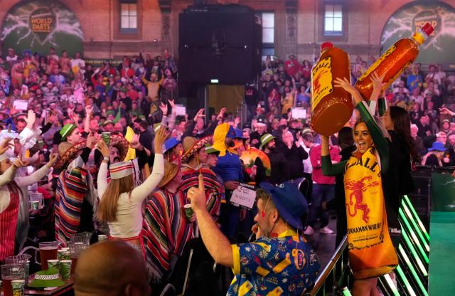Staff with plastic bottles of whisky egg on the crowd during the World Darts Championship at Alexandra Palace in London on December 28, 2025. Dressed as Elvis, Asterix or Snow White, usually with a drink in hand, fans transform London's Alexandra Palace into an overheated darts temple for a world championship that resembles a Christmas carnival. Some are there for the darts, but for others the annual event is about dressing up, having a drink and soaking up the raucous atmosphere. (Photo by CARLOS JASSO / AFP)