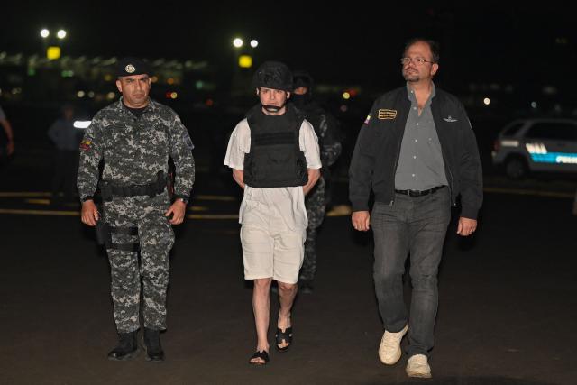 Roberto Alvarez (C), alias "El Gerente," an Ecuadorean alleged leader of a Colombian guerrilla group, is escorted by the Commander-in-Chief of Ecuador's National Police, Pablo Davila (L) and Ecuador's Interior Minister John Reimberg, upon landing at the Police base in Jose Joaquin de Olmedo International Airport in Guayaquil, Ecuador, on December 29, 2025, after being transferred from the United Arab Emirates. Alvarez, wanted by Ecuadorean authorities for the killing of 11 soldiers, has been identified by the government as the head of the Border Commands, a dissident faction of the now-defunct Colombian guerrilla group FARC that did not adhere to the 2016 peace agreement. (Photo by Marcos PIN / AFP)