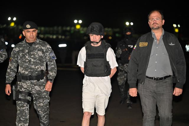 Roberto Alvarez (C), alias "El Gerente," an Ecuadorean alleged leader of a Colombian guerrilla group, is escorted by the Commander-in-Chief of Ecuador's National Police, Pablo Davila (L) and Ecuador's Interior Minister John Reimberg, upon landing at the Police base in Jose Joaquin de Olmedo International Airport in Guayaquil, Ecuador, on December 29, 2025, after being transferred from the United Arab Emirates. Alvarez, wanted by Ecuadorean authorities for the killing of 11 soldiers, has been identified by the government as the head of the Border Commands, a dissident faction of the now-defunct Colombian guerrilla group FARC that did not adhere to the 2016 peace agreement. (Photo by Marcos PIN / AFP)
