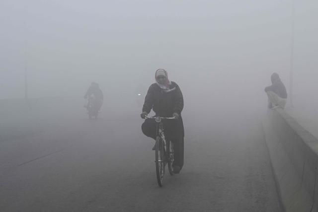 A man with his face covered in cloth rides a bicycle along a street amid dense smog in Lahore on December 30, 2025. (Photo by Arif ALI / AFP)