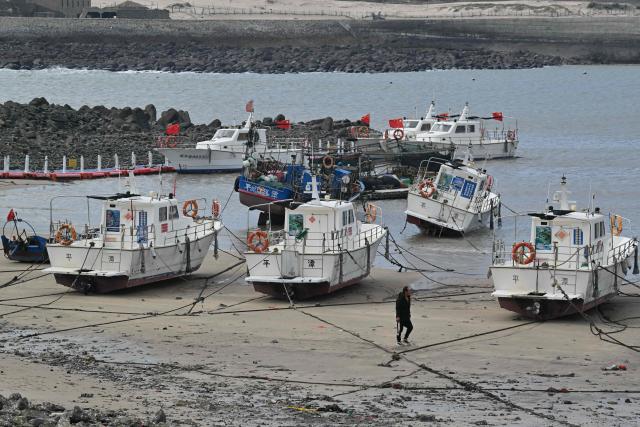 A man walks past boats on a beach during low tide on Pingtan island, the closest point to Taiwan, in eastern China’s Fujian province on December 30, 2025. China's military drills around Taiwan entered their second day on December 30, the sixth major manoeuvres Beijing has held near the self-ruled island in recent years. (Photo by ADEK BERRY / AFP)