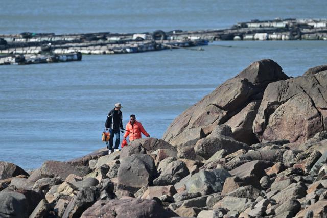 Anglers walk on the rocks on Pingtan island, the closest point to Taiwan, in eastern China’s Fujian province on December 30, 2025. China's military drills around Taiwan entered their second day on December 30, the sixth major manoeuvres Beijing has held near the self-ruled island in recent years. (Photo by ADEK BERRY / AFP)
