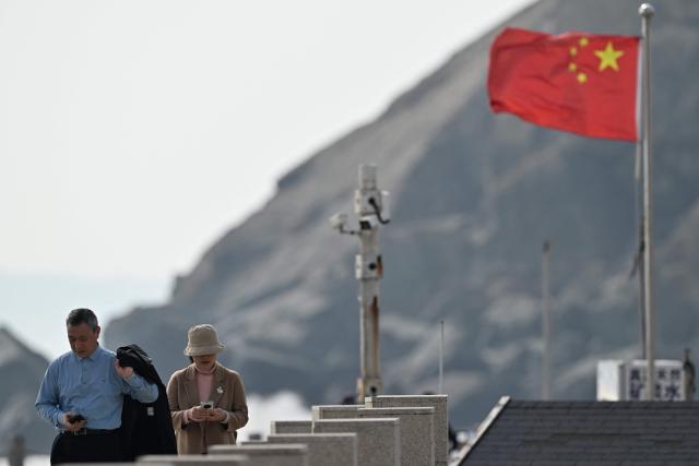 Visitors walk past a surveillance camera post (C) and a Chinese flag (R) on Pingtan island, the closest point to Taiwan, in eastern China’s Fujian province on December 30, 2025. China's military drills around Taiwan entered their second day on December 30, the sixth major manoeuvres Beijing has held near the self-ruled island in recent years. (Photo by ADEK BERRY / AFP)