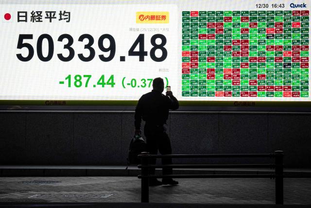 A man takes photographs of an electronic quotation board displaying the Nikkei Stock Average closing price on the Tokyo Stock Exchange in Tokyo on December 30, 2025. (Photo by Yuichi YAMAZAKI / AFP)