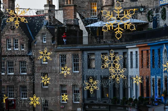 A woman in red (top L) looks out over festive lighting on Victoria Street in Edinburgh on December 30, 2025, ahead of the annual Hogmanay street party which culminates in a midnight fireworks display over the castle. An estimated 100,000 people from dozens of countries are expected in Edinburgh for the New Year events, the centrepiece of which is a street party and fireworks display on December 31. (Photo by Andy Buchanan / AFP)