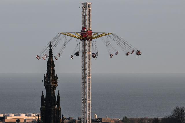 People take part in a carnival ride, just some of the festive attractions on Princess Street in Edinburgh on December 30, 2025, ahead of the annual Hogmanay street party which culminates in a midnight fireworks display over the castle. An estimated 100,000 people from dozens of countries are expected in Edinburgh for the New Year events, the centrepiece of which is a street party and fireworks display on December 31. (Photo by Andy Buchanan / AFP)