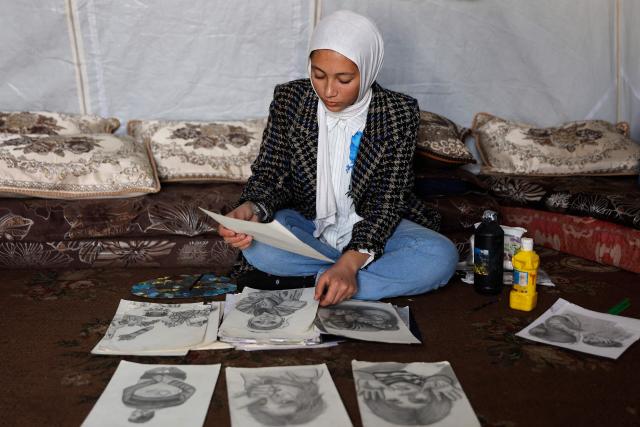 Fifteen-year-old displaced Palestinian Sarah Saada, who fled Beit Lahia in the northern Gaza Strip during Israeli bombardment, goes through some of her drawings inside her tent in Gaza City on December 30, 2025. Beginning in October, a fragile ceasefire has so far halted two years of war between Israel and Hamas in the Gaza Strip despite both sides trading accusations of truce violations. (Photo by Omar AL-QATTAA / AFP)