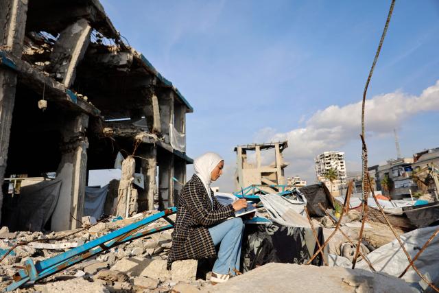 Fifteen-year-old displaced Palestinian Sarah Saada, who fled Beit Lahia in the northern Gaza Strip during Israeli bombardment, paints amid the rubble of destroyed buildings in Gaza City, on December 30, 2025. (Photo by Omar AL-QATTAA / AFP)