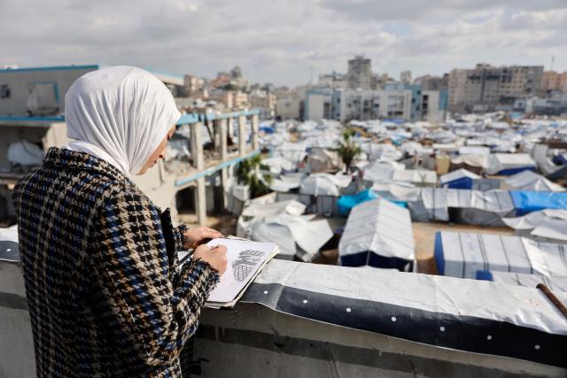 Fifteen-year-old displaced Palestinian Sarah Saada, who fled Beit Lahia in the northern Gaza Strip during Israeli bombardment, draws as she stands next to her tent overlooking a camp for the displaced in Gaza City on December 30, 2025. Beginning in October, a fragile ceasefire has so far halted two years of war between Israel and Hamas in the Gaza Strip despite both sides trading accusations of truce violations. (Photo by Omar AL-QATTAA / AFP)