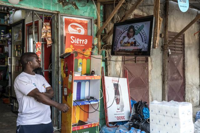 A local resident looks at a television screen displaying General Directorate of Elections (DGE) Director Djenabou Toure announcing the official partial results of Guinea’s presidential election near the DGE offices in Conakry, on December 30, 2025. Guinea's junta chief, who had pledged not to run for office after seizing power four years ago, has a large lead in presidential elections held at the weekend, according to initial results published late December 29. (Photo by PATRICK MEINHARDT / AFP)