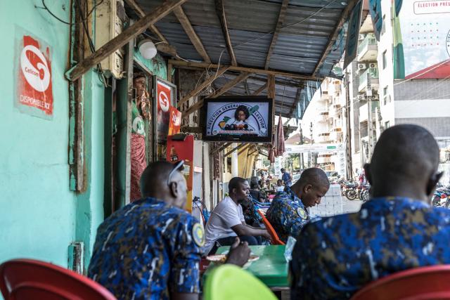 Guinean police officers sit next to a television displaying General Directorate of Elections (DGE) Director Djenabou Toure announcing the official partial results of Guinea’s presidential election near the DGE offices in Conakry, on December 30, 2025. Guinea's junta chief, who had pledged not to run for office after seizing power four years ago, has a large lead in presidential elections held at the weekend, according to initial results published late December 29. (Photo by PATRICK MEINHARDT / AFP)