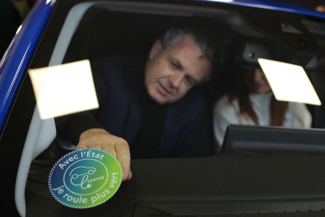 (FILES) French Minister for Ecological Transition and Territories' Cohesion Christophe Bechu displays the "social leasing" logo on the car's windshield after handing over a vehicle to the first beneficiary of the "social leasing", in Joinville-le-Pont, near Paris, on January 22, 2024. With just a few hours to go before the end of 2025, several hundred electric cars were still available to low-income households through the ‘social leasing’ scheme set up by the government for the second year running. (Photo by Thomas SAMSON / AFP)