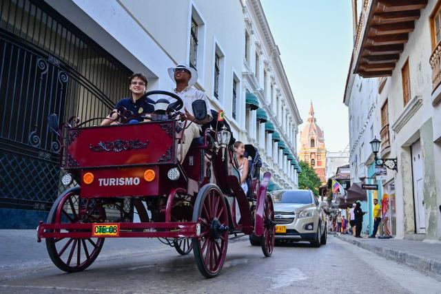 A coachman drives a new electric carriage as he transports tourists through the historic center of Cartagena, Colombia, on December 30, 2025. Traditional horse-drawn carriages will be banned starting December 29, 2025, in Cartagena, a tourist gem in Colombia, according to an announcement made by the local mayor on December 26. (Photo by Manuel PEDRAZA / AFP)