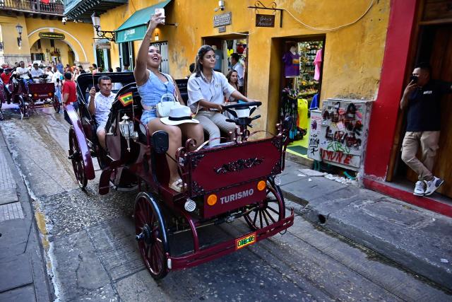 A female coachman drives a new electric carriage as she transports tourists through the historic center of Cartagena, Colombia, on December 30, 2025. Traditional horse-drawn carriages will be banned starting December 29, 2025, in Cartagena, a tourist gem in Colombia, according to an announcement made by the local mayor on December 26. (Photo by Manuel PEDRAZA / AFP)