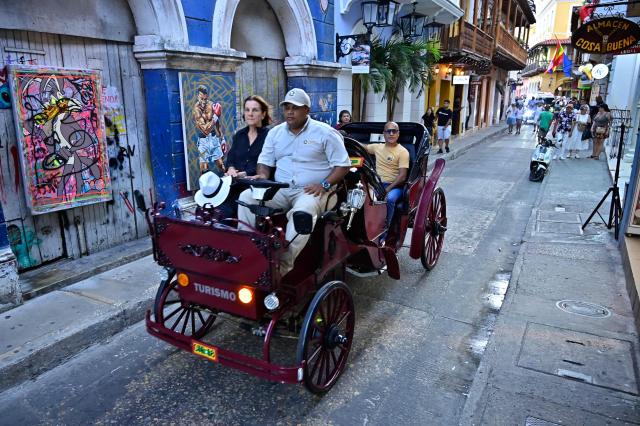 A coachman drives a new electric carriage as he transports tourists through the historic center of Cartagena, Colombia, on December 30, 2025. Traditional horse-drawn carriages will be banned starting December 29, 2025, in Cartagena, a tourist gem in Colombia, according to an announcement made by the local mayor on December 26. (Photo by Manuel PEDRAZA / AFP)