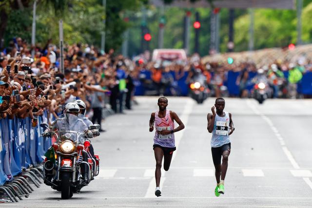 Ethiopian runner Muse Gizachew (L) overtakes Kenian runner Jonathan Kipkoech Kamosong before he crosses the finish line to win the men's 15km competition of the 100th edition of the Saint Silvestre road race in Sao Paulo, Brazil, on December 31, 2025. (Photo by Miguel SCHINCARIOL / AFP)