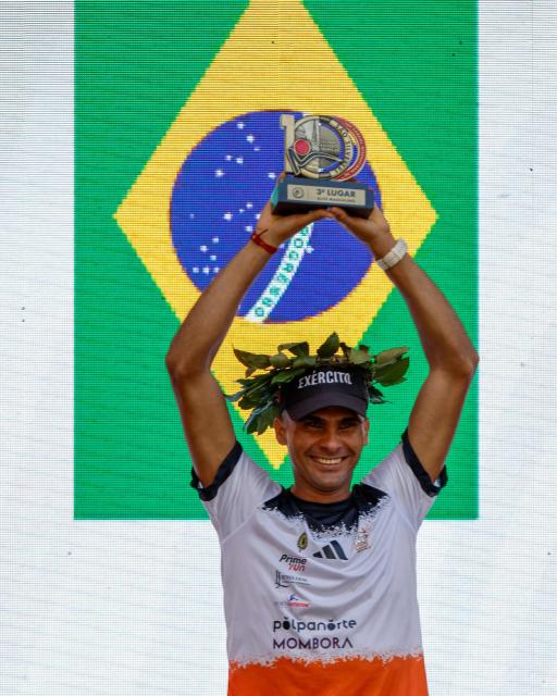 Brazilian runner Fabio Jesus Correia celebrates in the podium after getting the third place in the men's 15km competition of the 100th edition of the Saint Silvestre road race in Sao Paulo, Brazil, on December 31, 2025. (Photo by Miguel SCHINCARIOL / AFP)