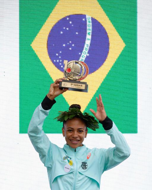Brazilian runner Nubia de Oliveira celebrates in the podium after getting the third place in the women's 15km competition of the 100th edition of the Saint Silvestre road race in Sao Paulo, Brazil, on December 31, 2025. (Photo by Miguel SCHINCARIOL / AFP)