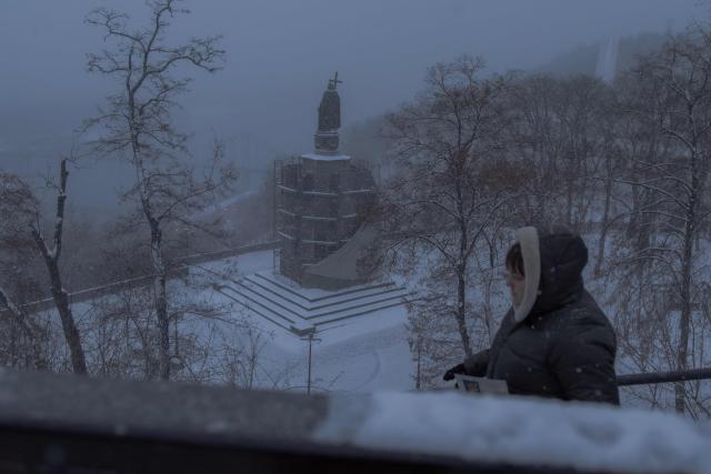 A pedestrian walks through Saint Volodymyr Hill Park with the monument to St. Volodymyr in the background during a snowy day on New Year's Eve in Kyiv on December 31, 2025, amid the Russian invasion of Ukraine. (Photo by Roman PILIPEY / AFP)