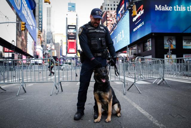 A New York City Police Department (NYPD) officer and dog stand watch ahead of tonight's New Year's Eve celebrations in Times Square, New York on December 31, 2025. (Photo by Kena BETANCUR / AFP)