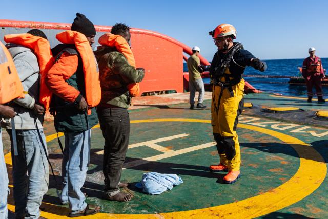 A crew member of the “Ocean Viking” rescue ship demonstrates how to wear a life jacket to migrants as they prepare to evacuate migrants from the oil tanker the 'Maridive 703' to RHIBs (Rigid inflatable boats) in the search-and-rescue zone of the international waters between Malta and Tunisia, on December 31, 2025. 33 migrants were rescued by crew members of the migrants rescue ship "Ocean Viking" operated by the French NGO SOS Mediterranee. They had been stranded on the oil tanker the 'Maridive 703' since their initial rescue 5 days ago in the joint search zone between Malta and Tunisia in international Mediterranean waters. (Photo by Sameer Al-DOUMY / AFP)